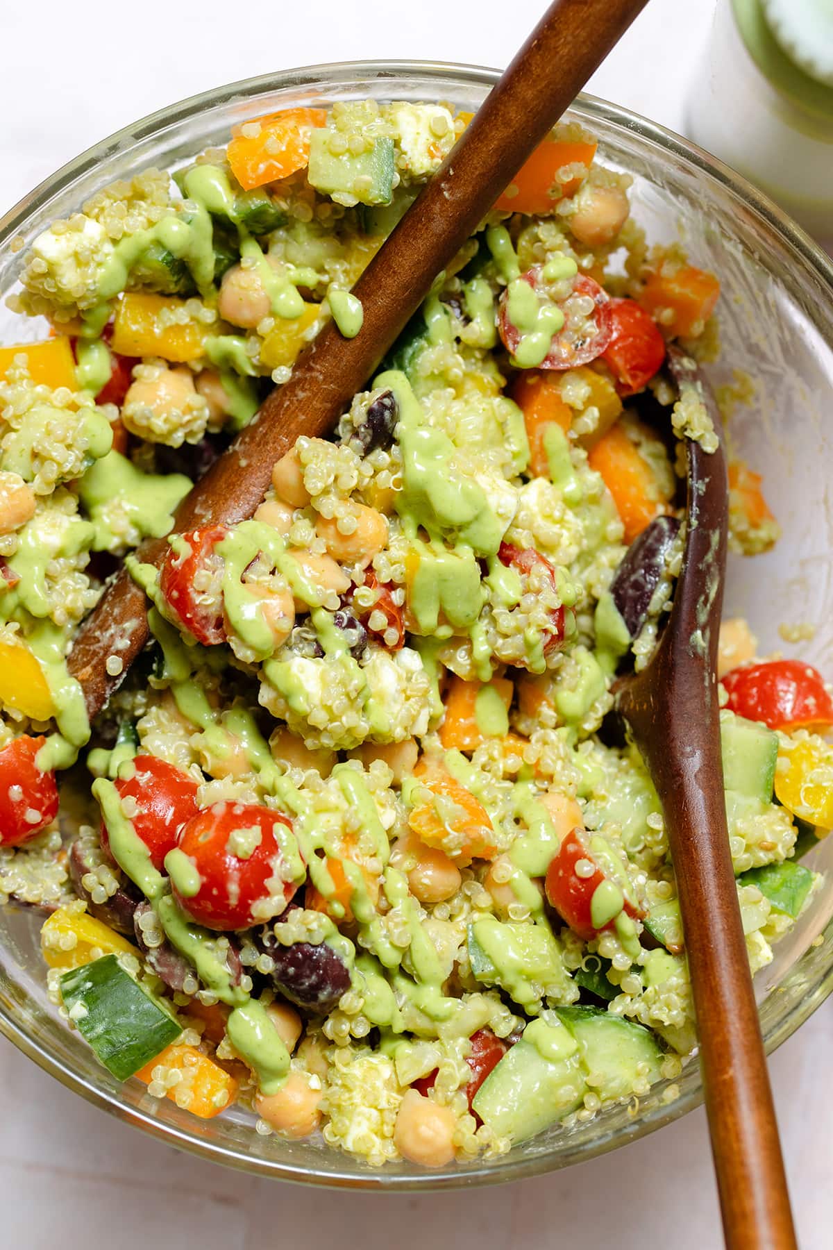 Quinoa chickpea salad with colorful vegetables in a large glass bowl with two wooden spoons.
