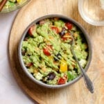 Colorful vegetable quinoa salad with green avocado dressing in a ceramic bowl on a wooden serving plate.