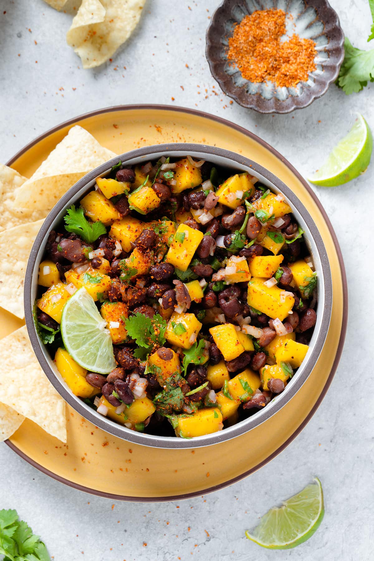 Black beans and mango salsa in a ceramic bowl on a yellow plate garnished with a slice of lime.