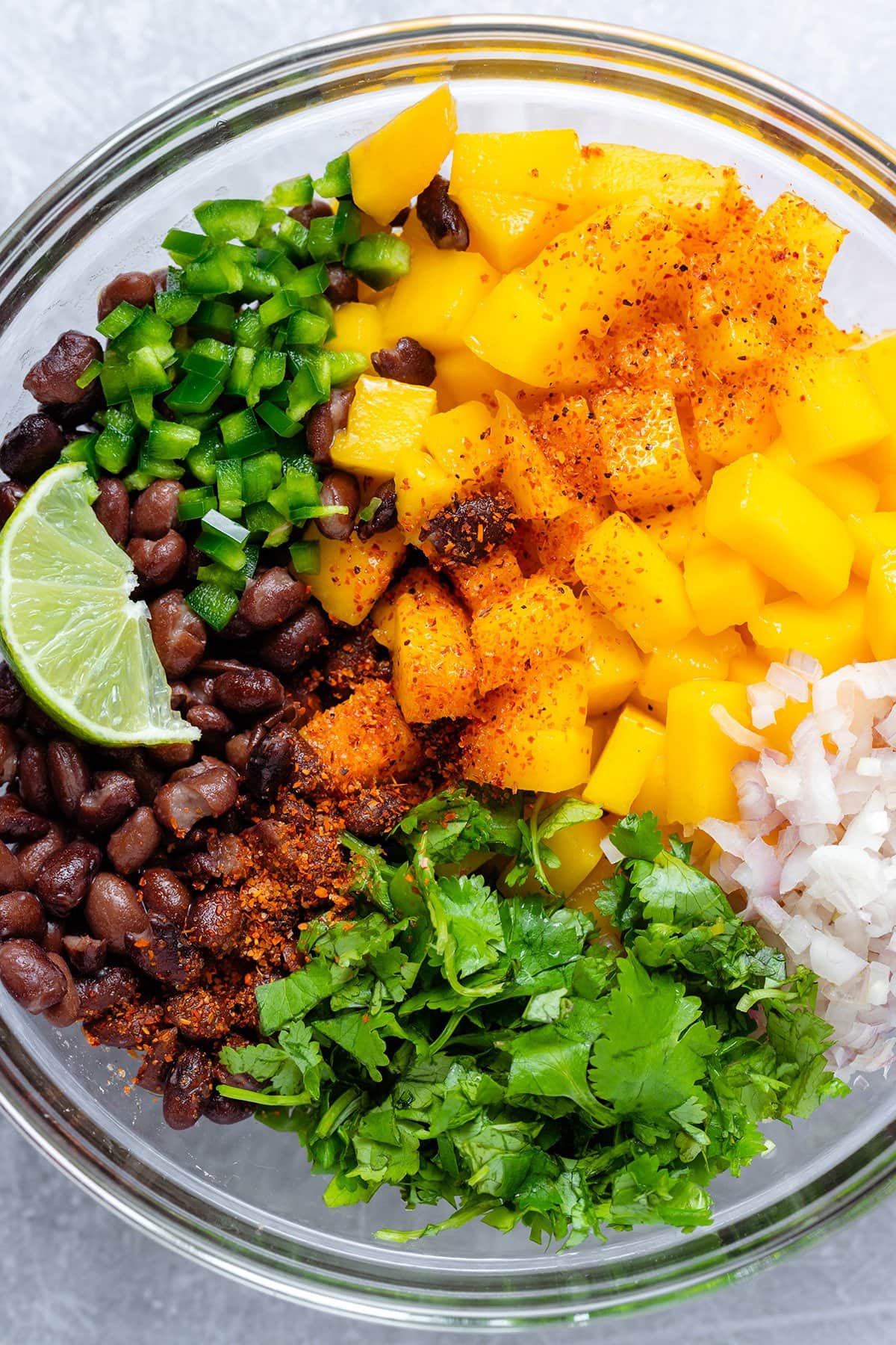 All ingredients for salsa like black beans, diced mango, and fresh cilantro in a glass mixing bowl.