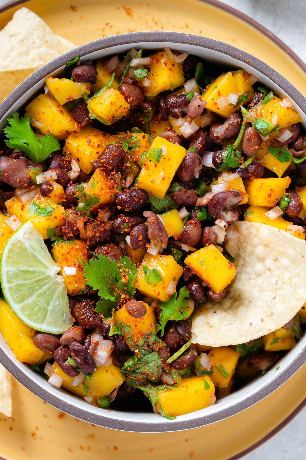 Black beans and mango salsa with fresh parsley in a ceramic bowl on a yellow plate garnished with a slice of lime.