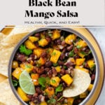 Black beans and mango salsa with fresh parsley in a ceramic bowl on a yellow plate garnished with a slice of lime.