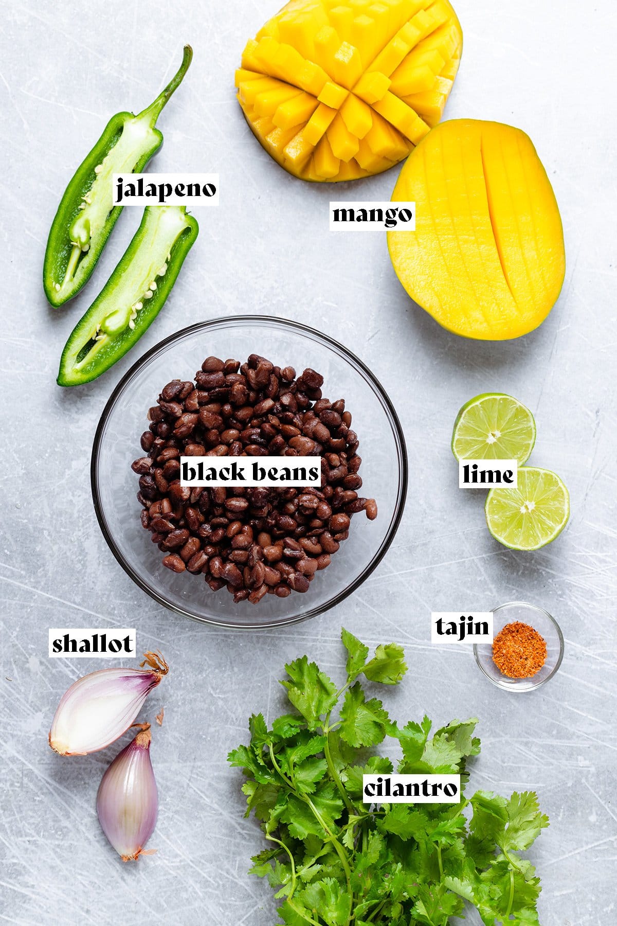 Ingredients for black bean mango salsa like diced mango, black beans, jalapeno, and lime laid out on a metal backgroud.