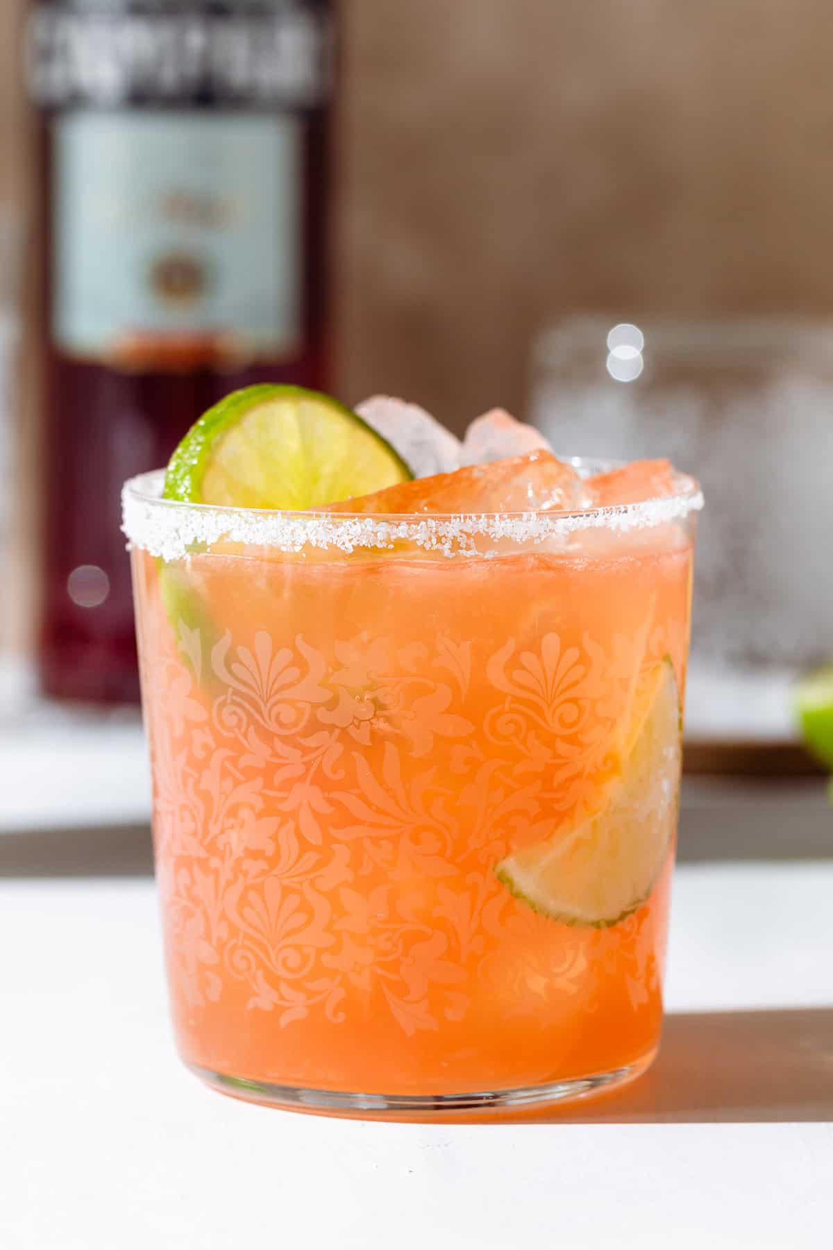 Orange drink in a short glass filled with ice garnished with a lime slice and salt around the rim.