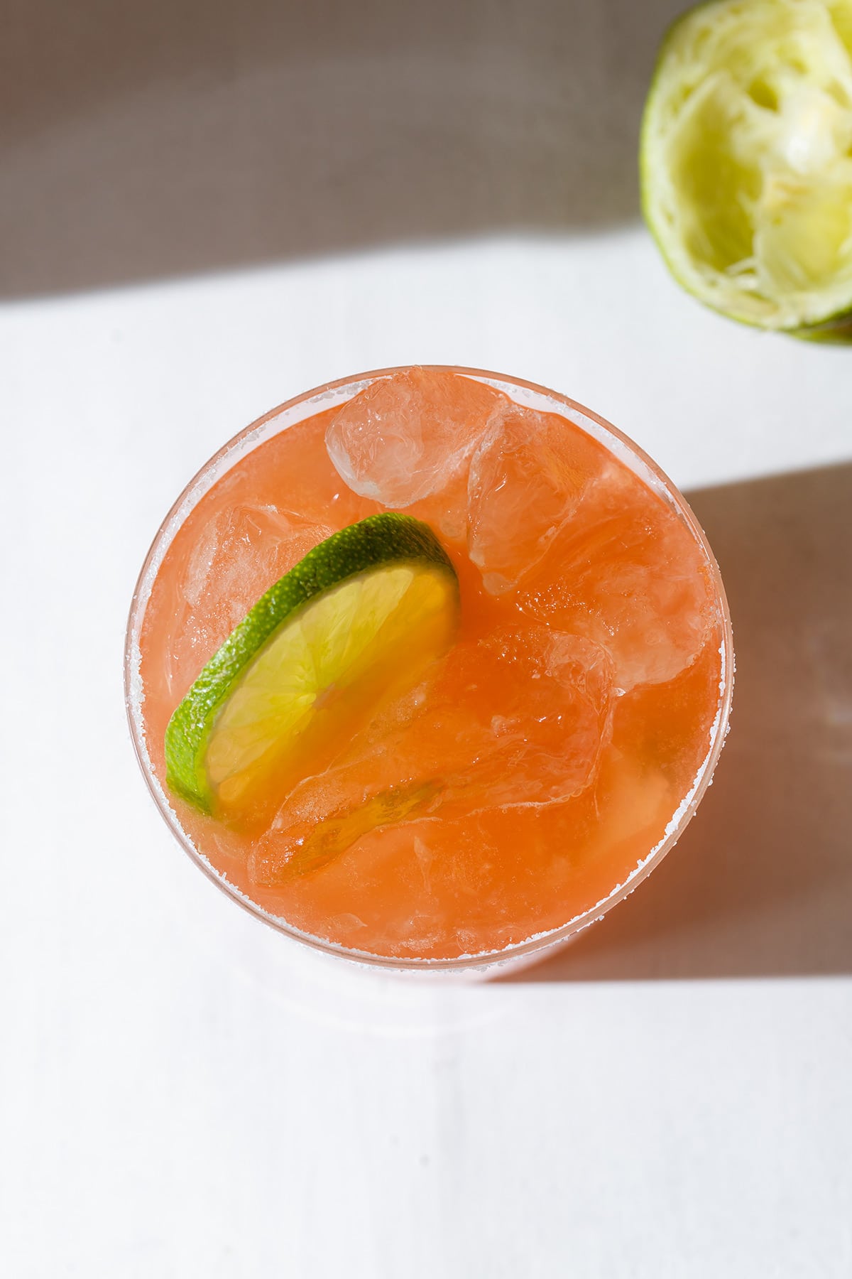 Orange drink in a short glass filled with ice garnished with a lime slice.