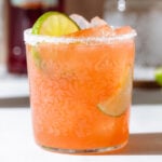 Orange drink in a short glass filled with ice garnished with a lime slice and salt around the rim.