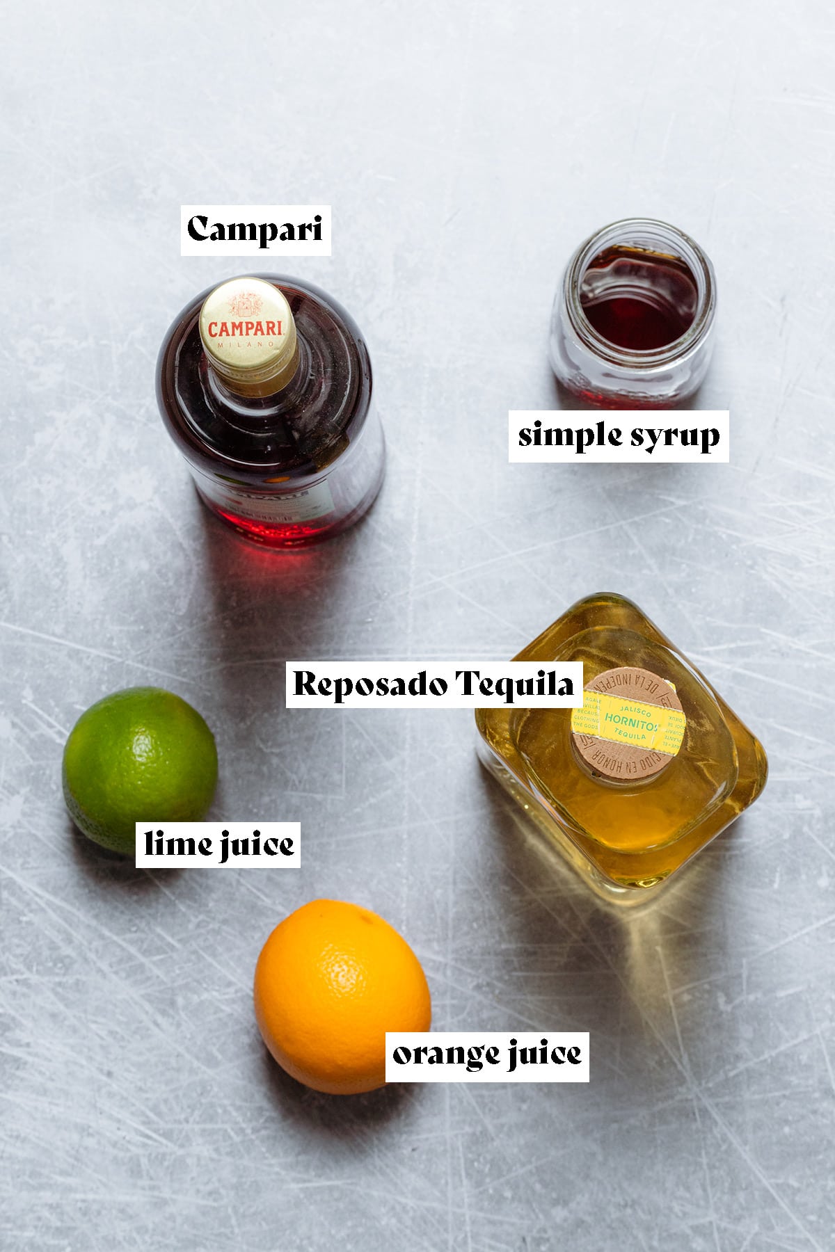 Ingredients for a Campari margarita like tequila and Campari laid out on a metal background.