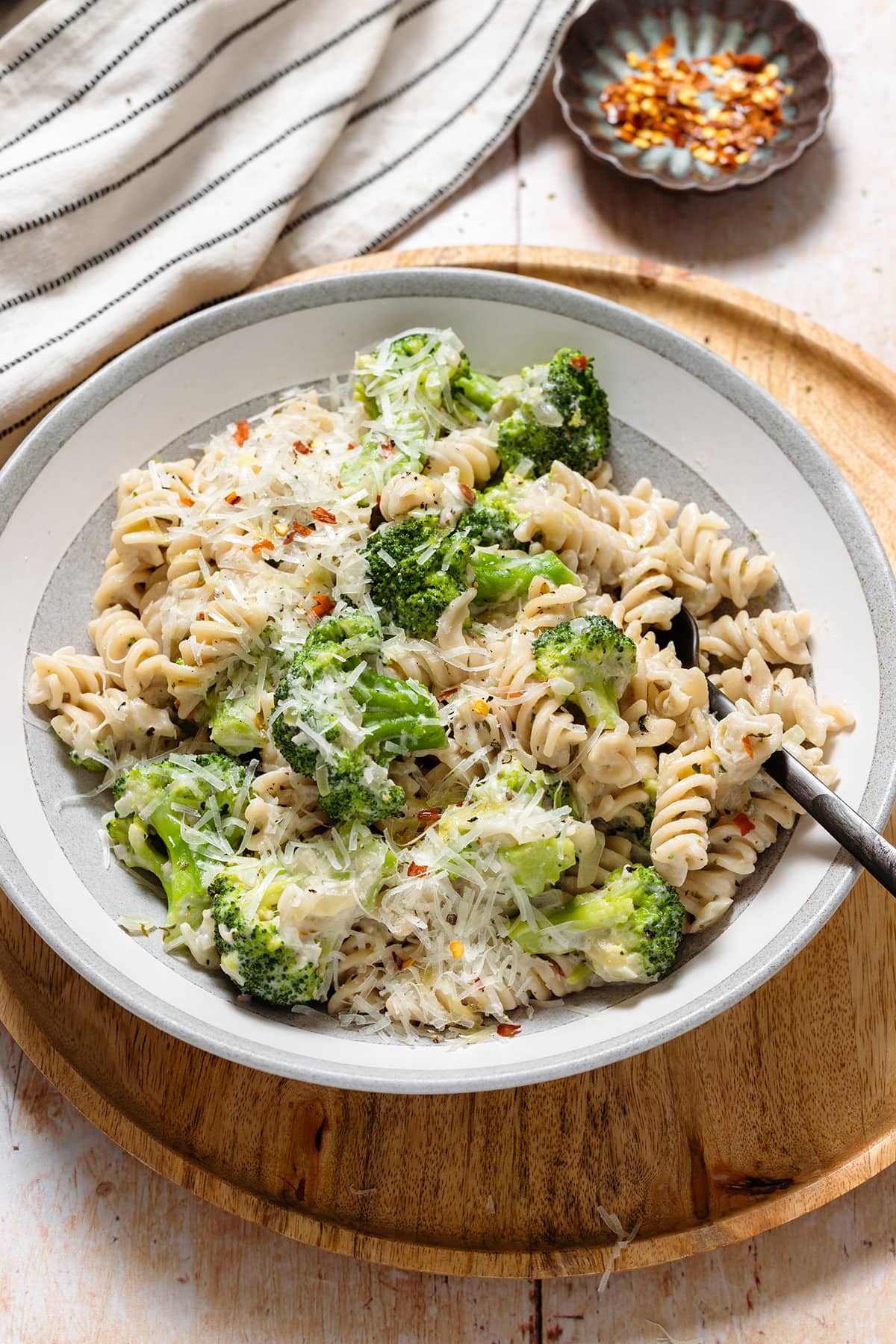 Pasta with creamy white sauce, broccoli, and grated pecorino in a wide grey bowl.