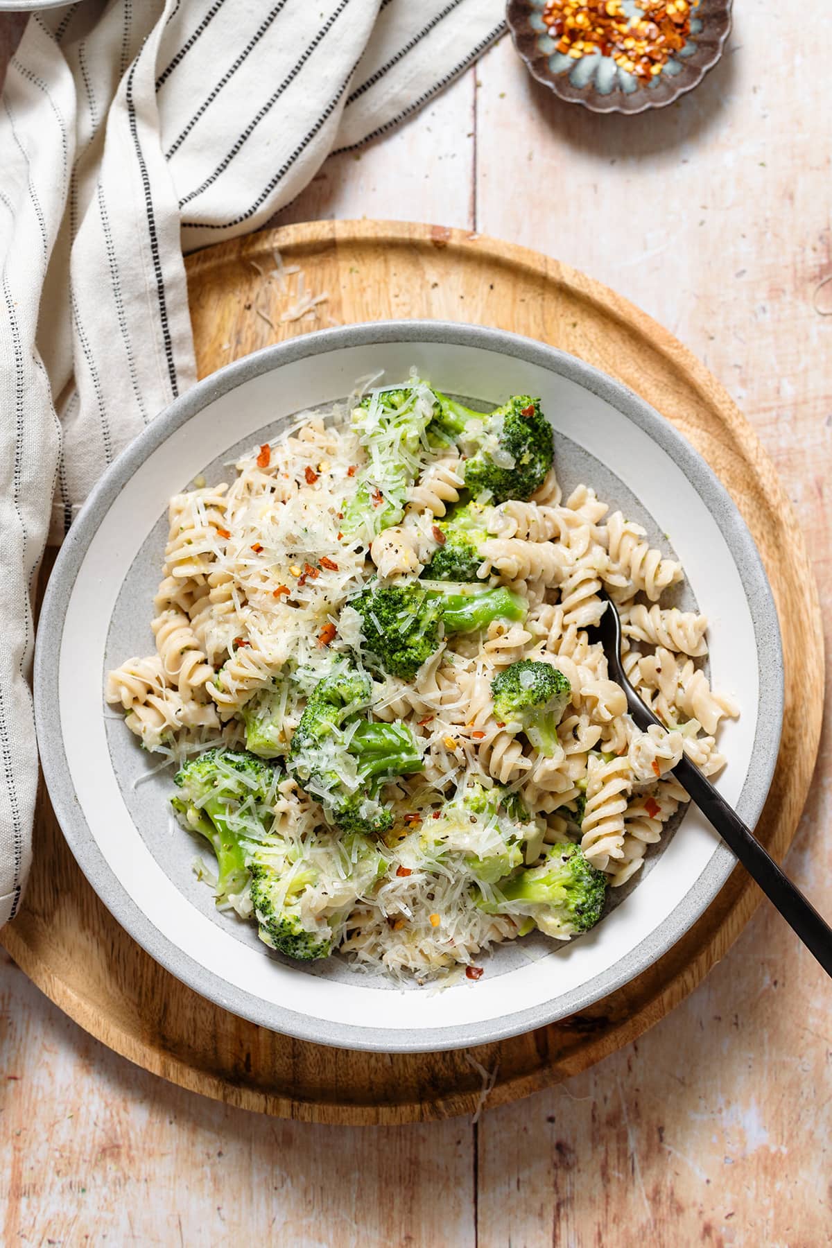 Pasta with creamy white sauce, broccoli, and grated pecorino in a wide grey bowl.