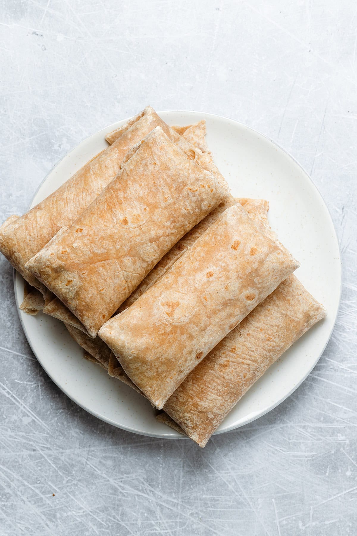 Five finished breakfast burritos on a white plate and metal background.