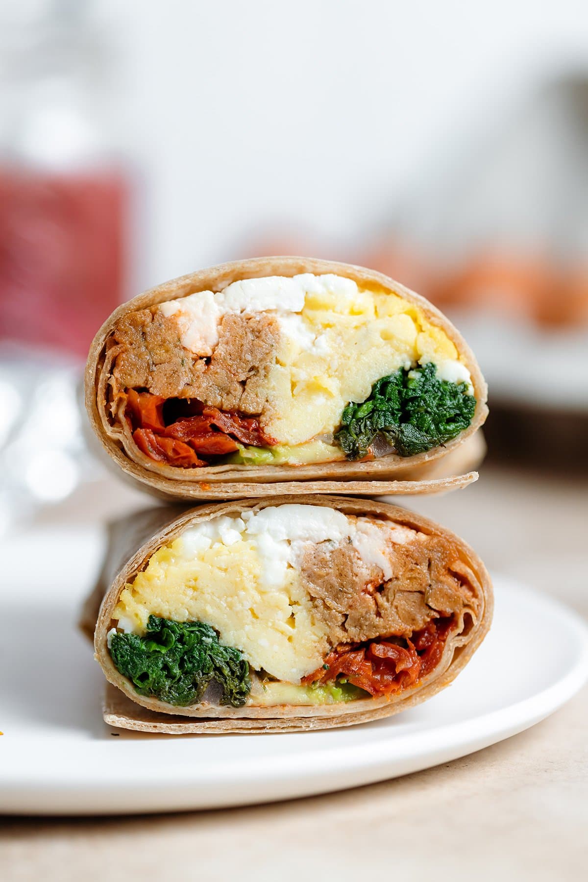 A breakfast burrito cut in half showing eggs, spinach, and sausage inside on a white plate.