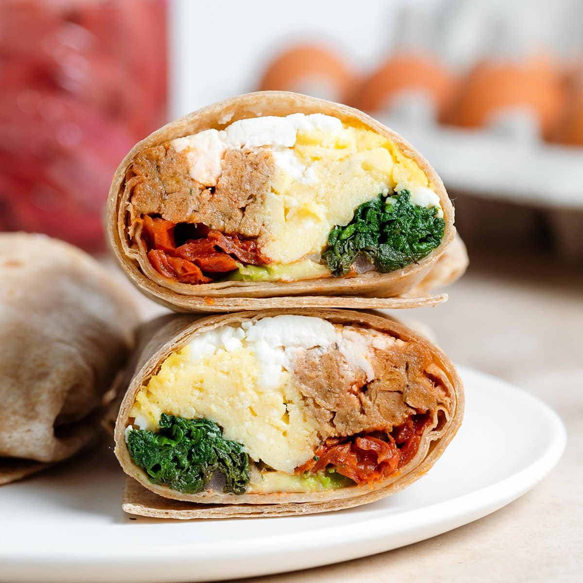 A breakfast burrito cut in half showing eggs, spinach, and sausage inside on a white plate.