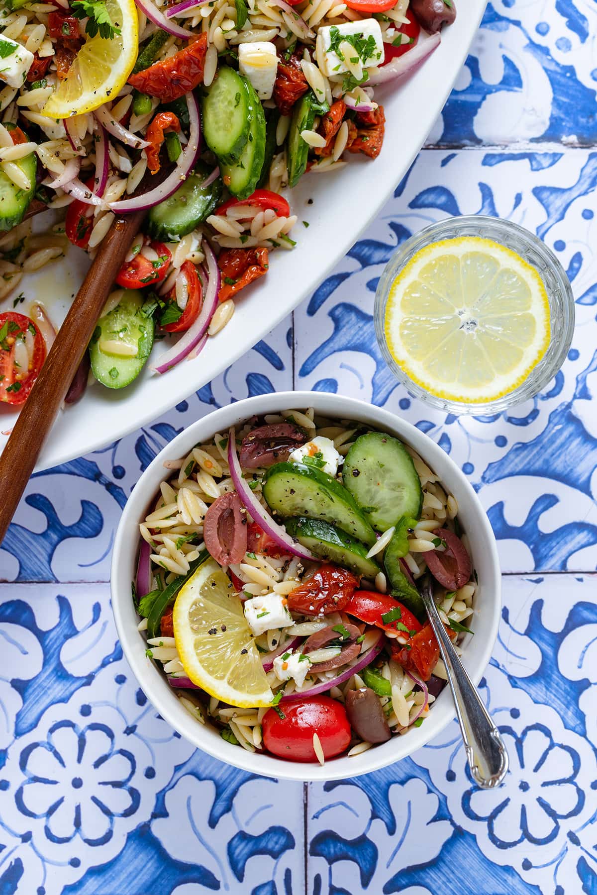 Greek orzo salad in a small white bowl with a fork garnished with a slice of lemon.