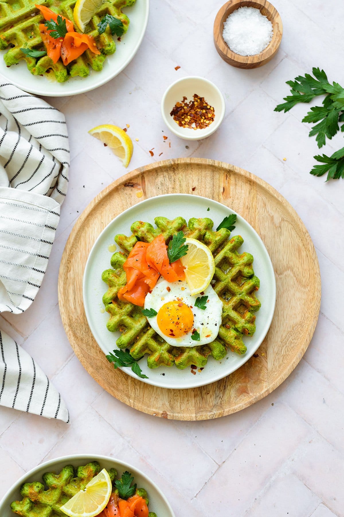 Green waffles on a white plate topped with a sunny side up egg, smoked salmon, fresh parsley, and a wedge of lemon.