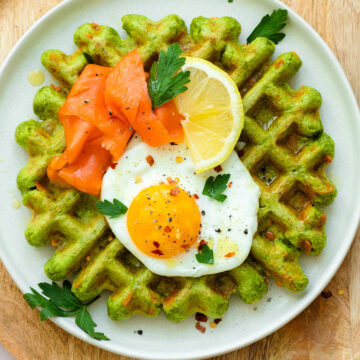 Green waffles on a white plate topped with a sunny side up egg and smoked salmon.