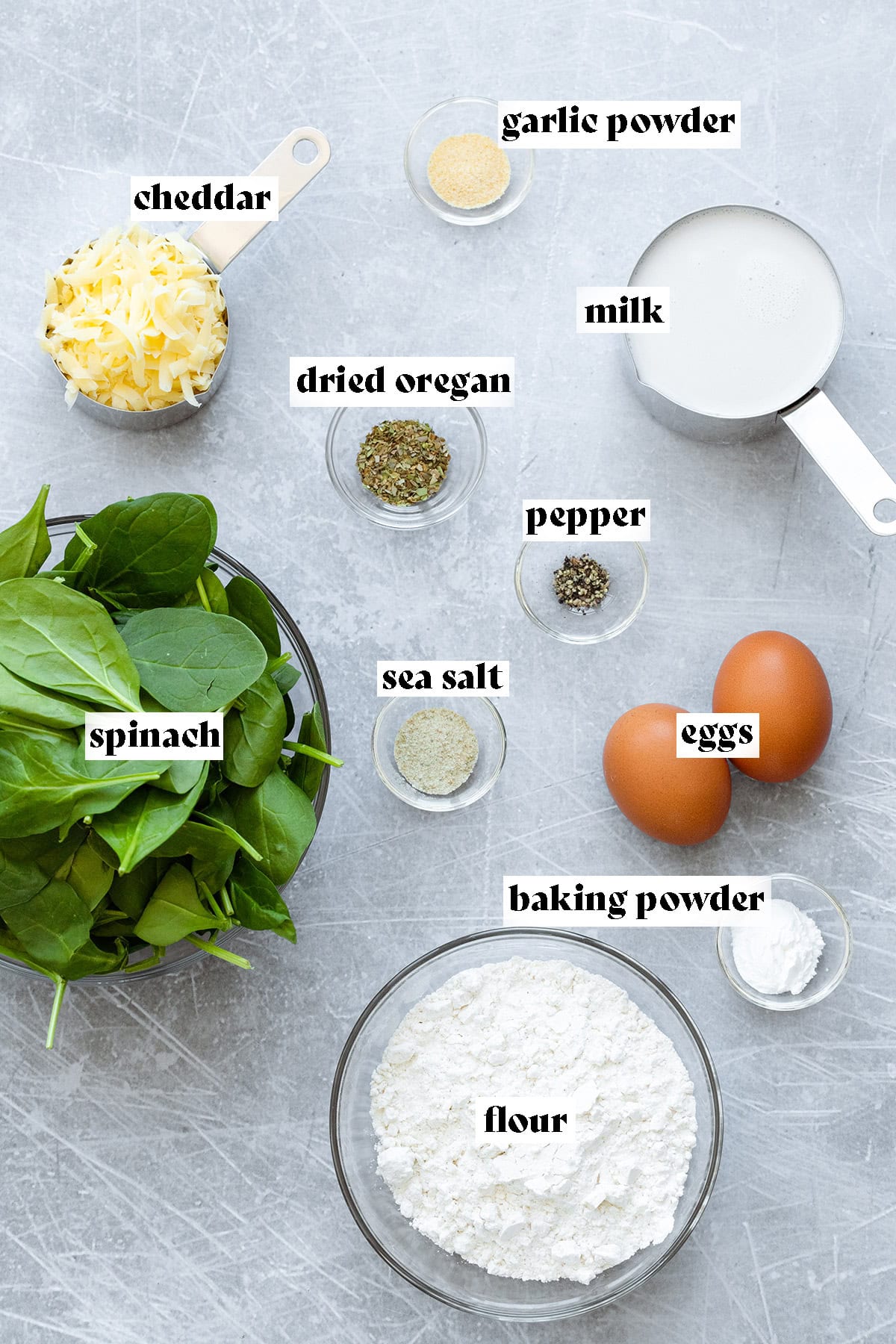 Ingredients for green waffles like spinach, flour, and eggs laid out on a metal background.