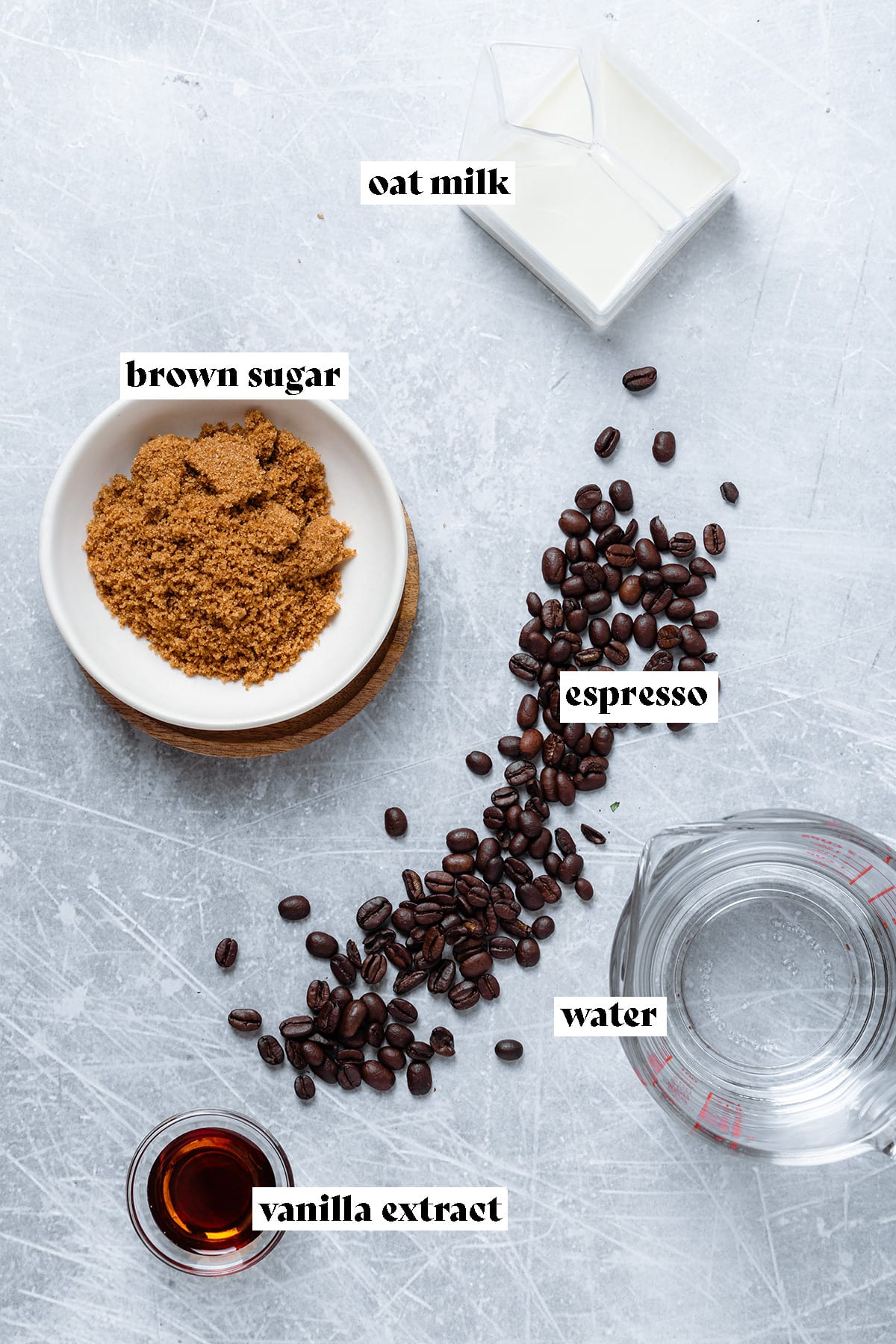 Brown sugar, water, oat milk, espresso beans, and vanilla extract laid out on a metal background.