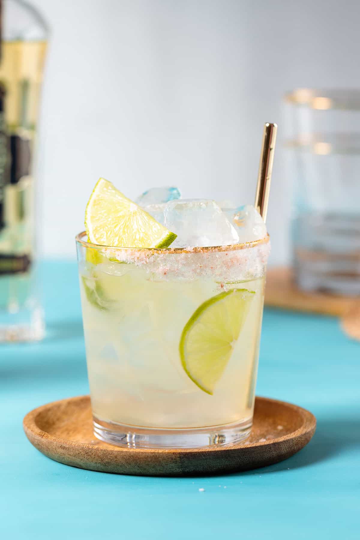 Elderflower margarita garnished with lime slices in a short glass on a blue background.