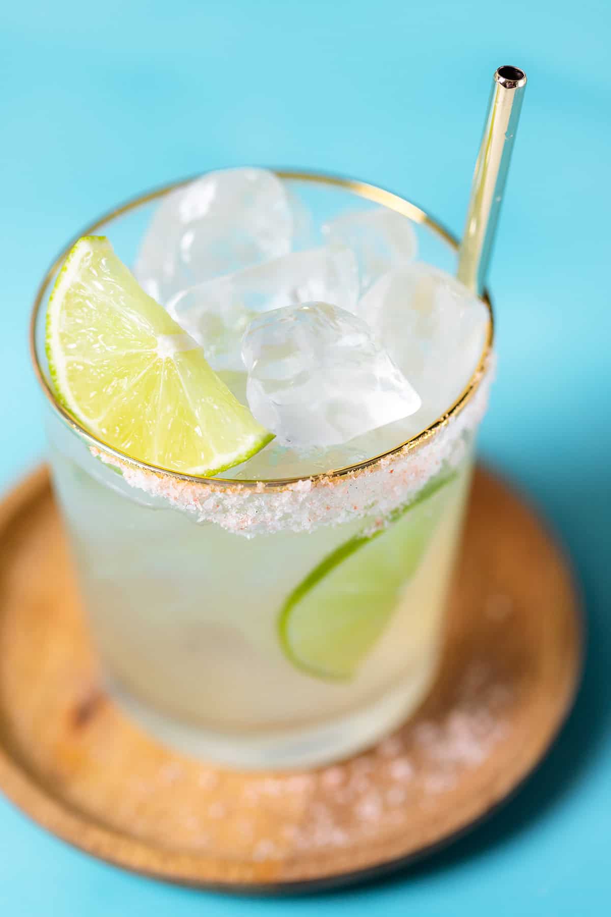 Elderflower margarita garnished with lime slices in a short glass on a blue background.