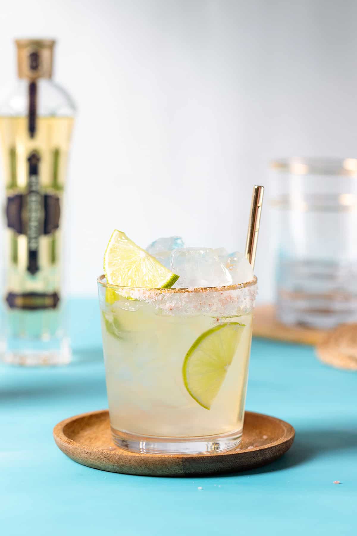 Elderflower margarita garnished with lime slices in a short glass on a blue background.