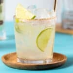 Elderflower margarita garnished with lime slices in a short glass on a blue background.