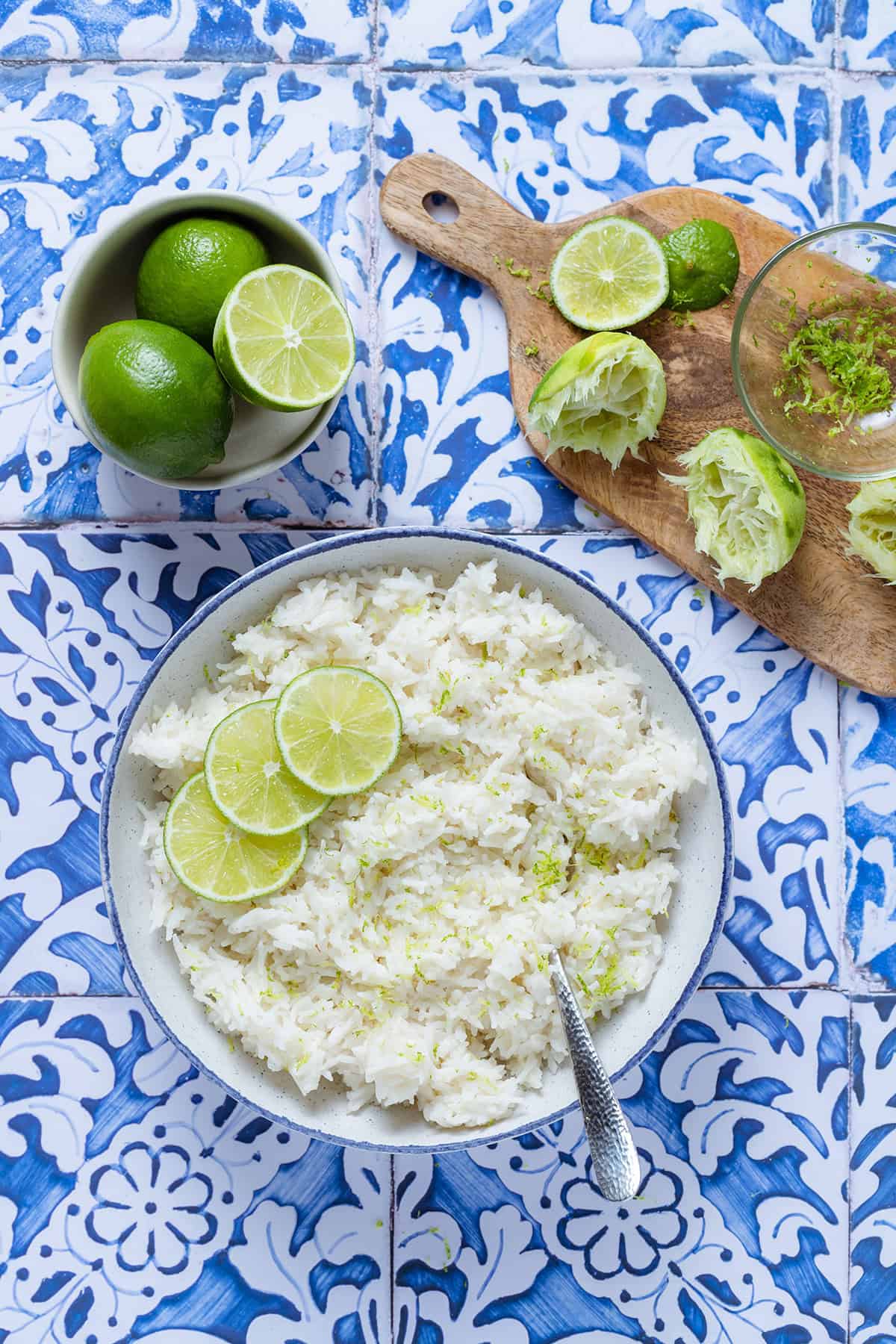 Coconut lime rice garnished with lime slices in a white bowl with a blue edge on a blue tile background.