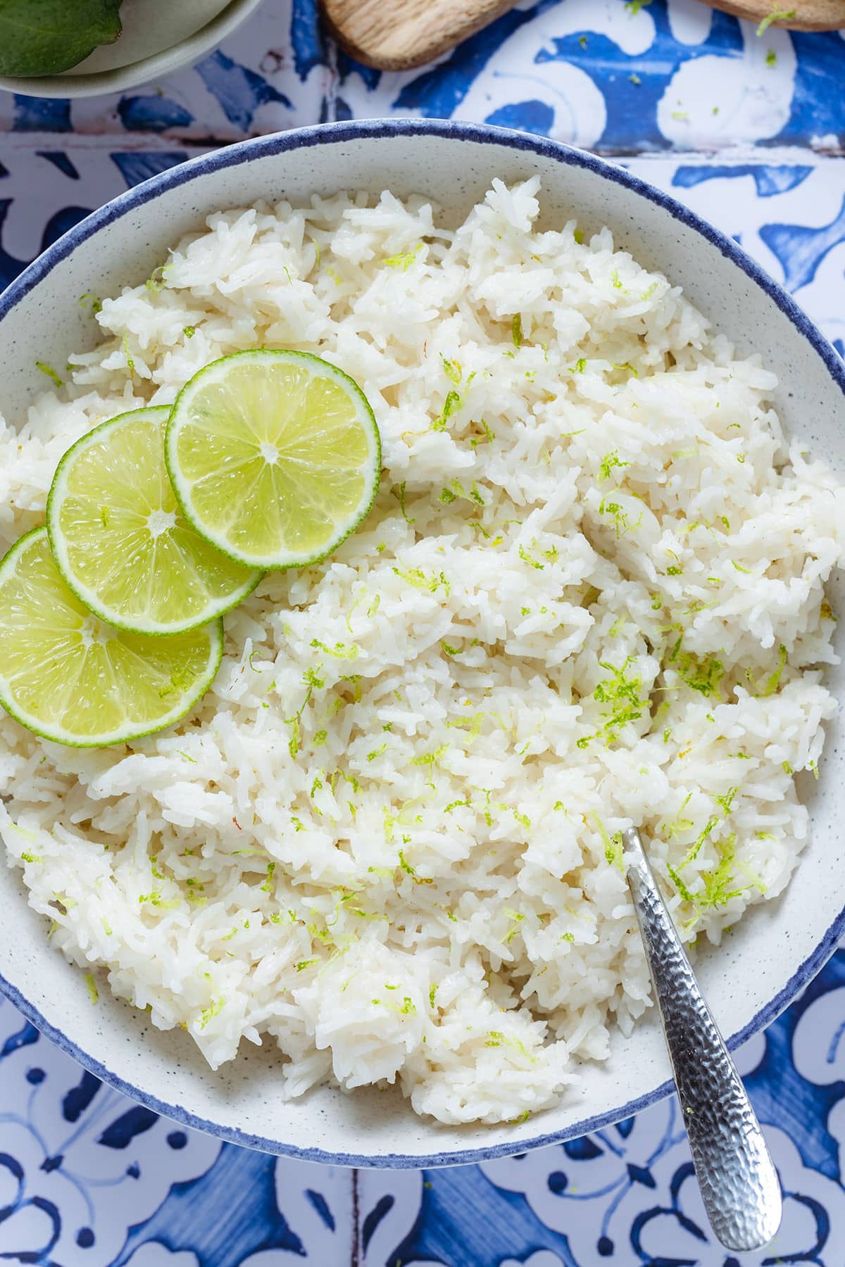 Coconut lime rice garnished with lime slices in a white bowl with a blue edge on a blue tile background.