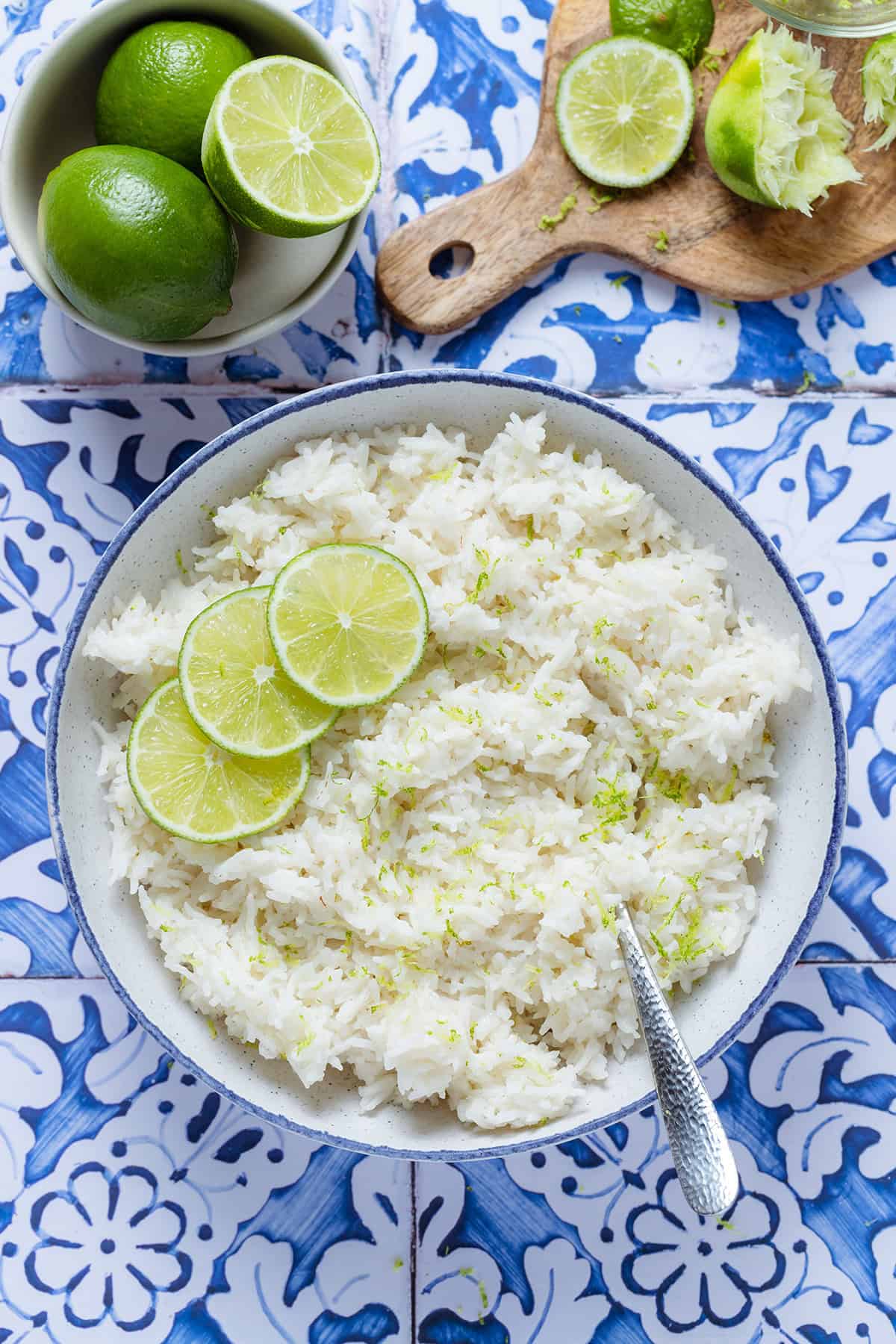 Coconut lime rice garnished with lime slices in a white bowl with a blue edge on a blue tile background.