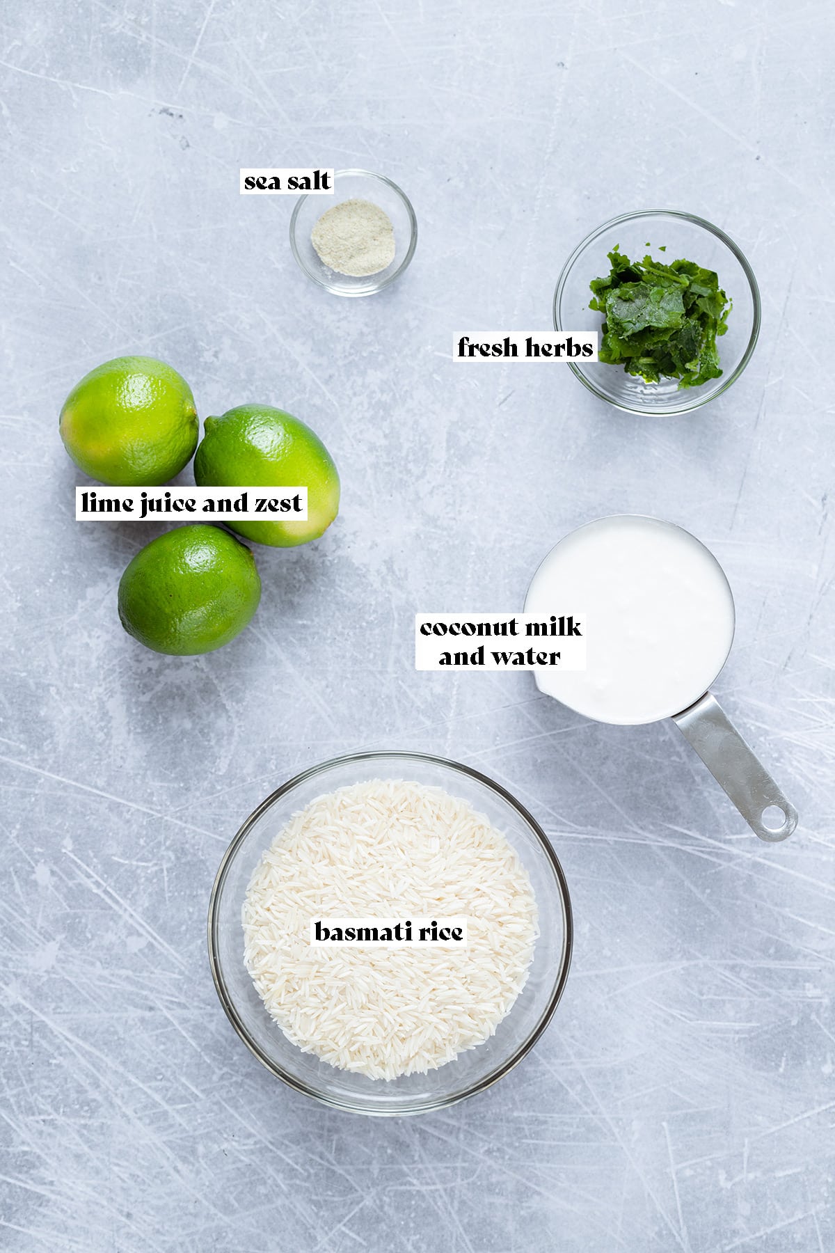 Ingredients for coconut lime rice like coconut milk, rice, and limes laid out on a metal background.