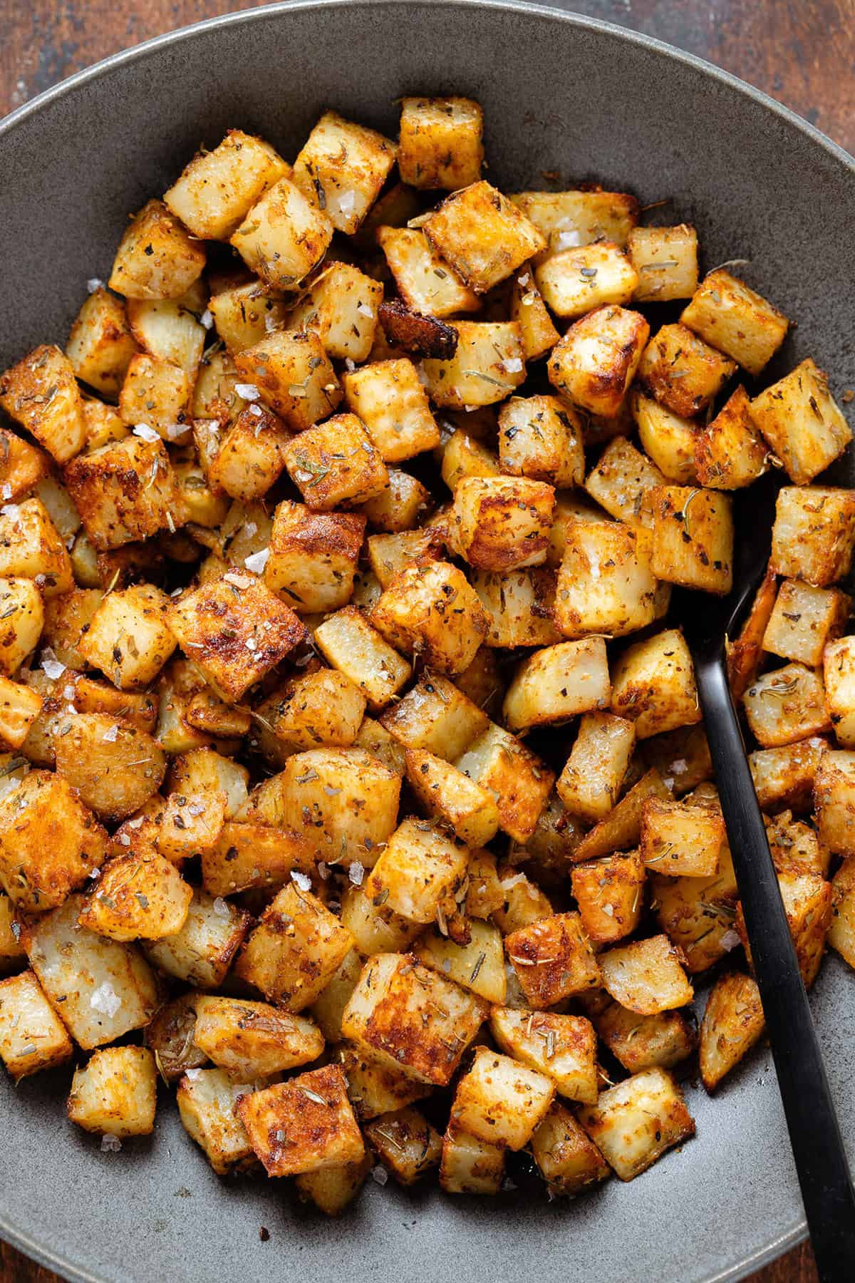 Roasted breakfast potatoes in a black bowl with a black serving spoon.