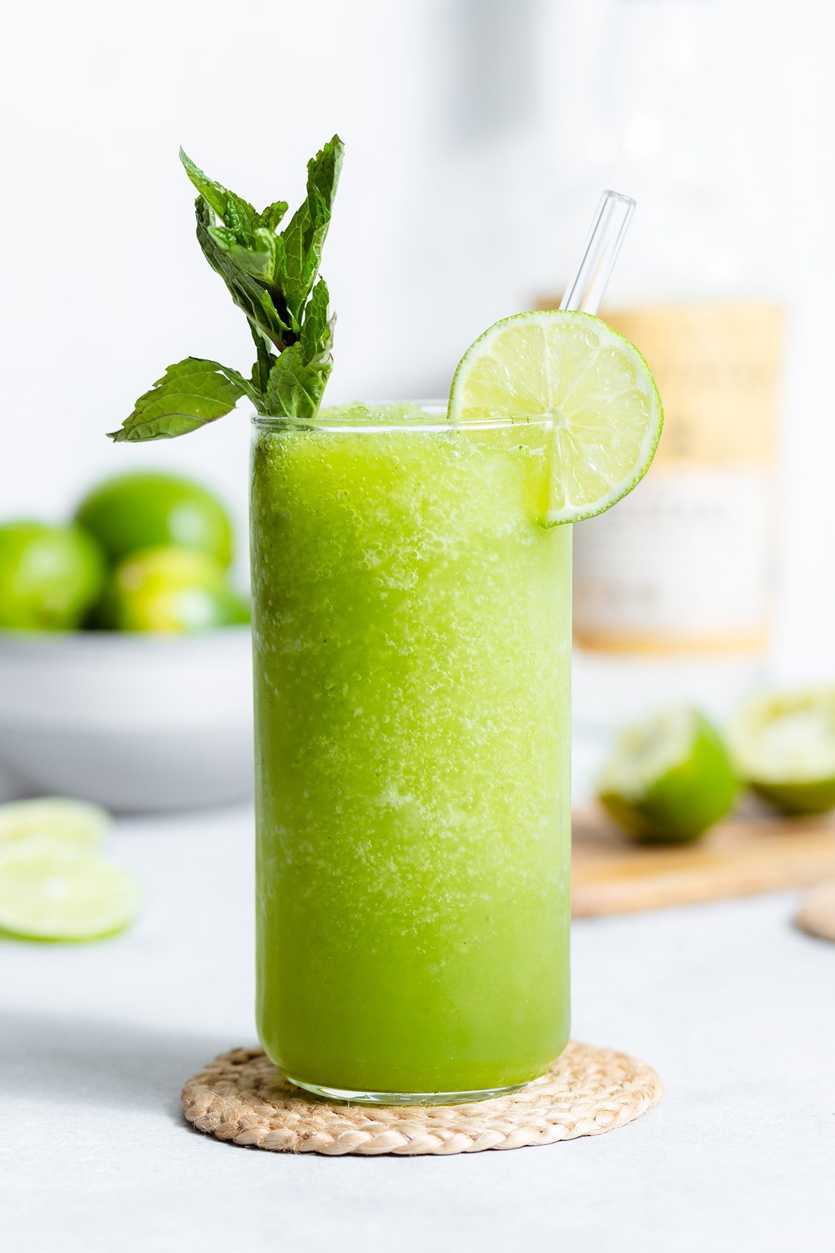 Blended mojito in a tall glass with a glass straw garnished with a lime slice and a string of mint.