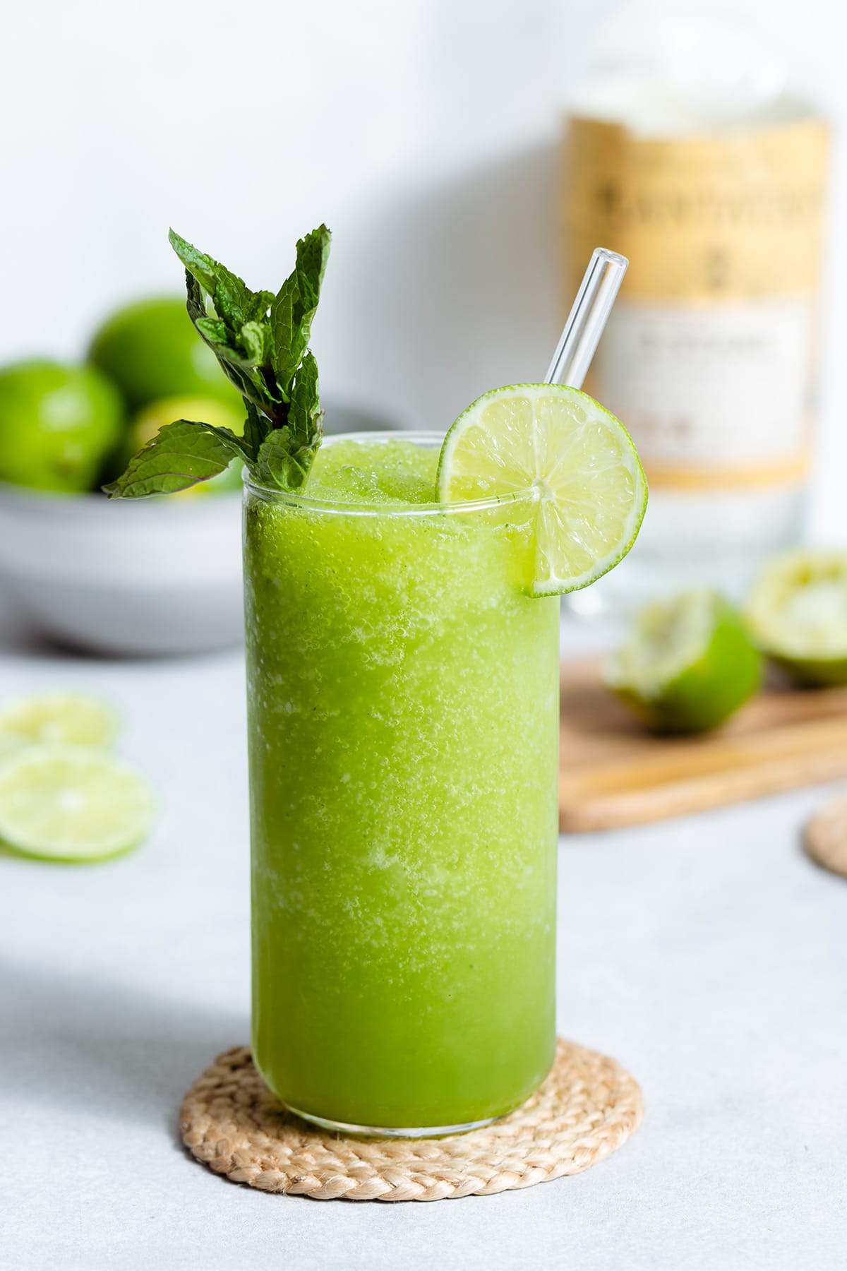 Blended mojito in a tall glass with a glass straw garnished with a lime slice and a string of mint.