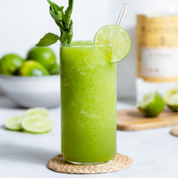 Blended mojito in a tall glass garnished with a lime slice and a string of mint.