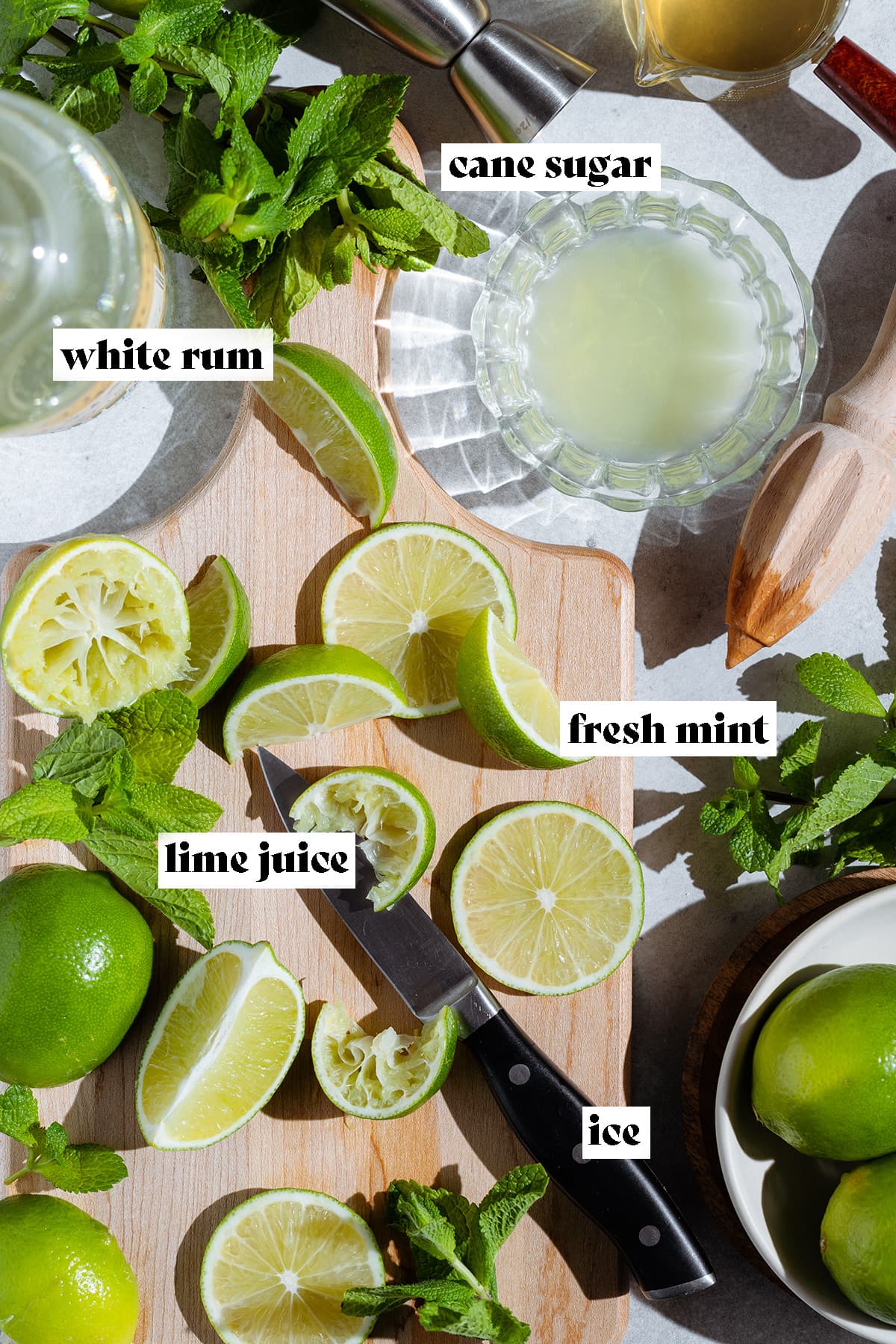 Wedges and slices of lime on a wooden cutting board with fresh mint and other mojito ingredients around the board.