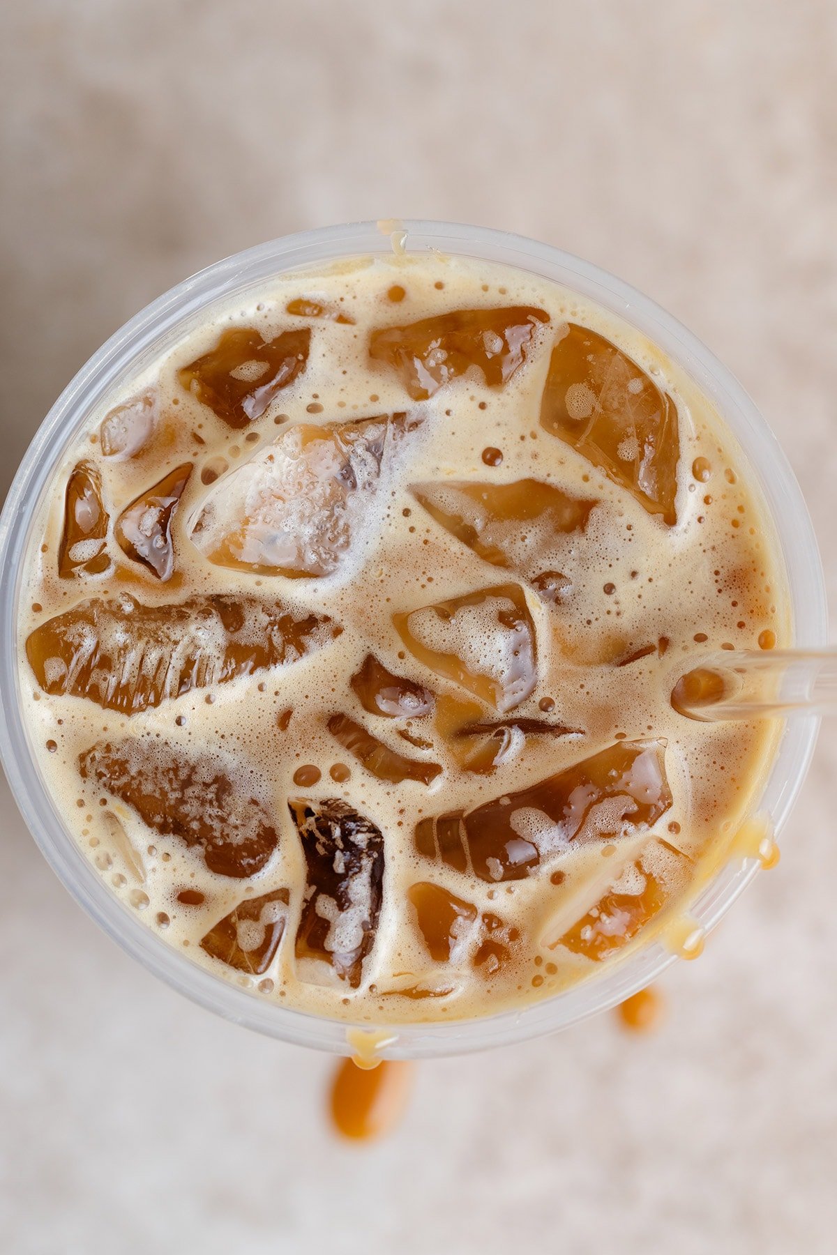 A close up of an iced coffee in a plastic cup with a glass straw shot from above.