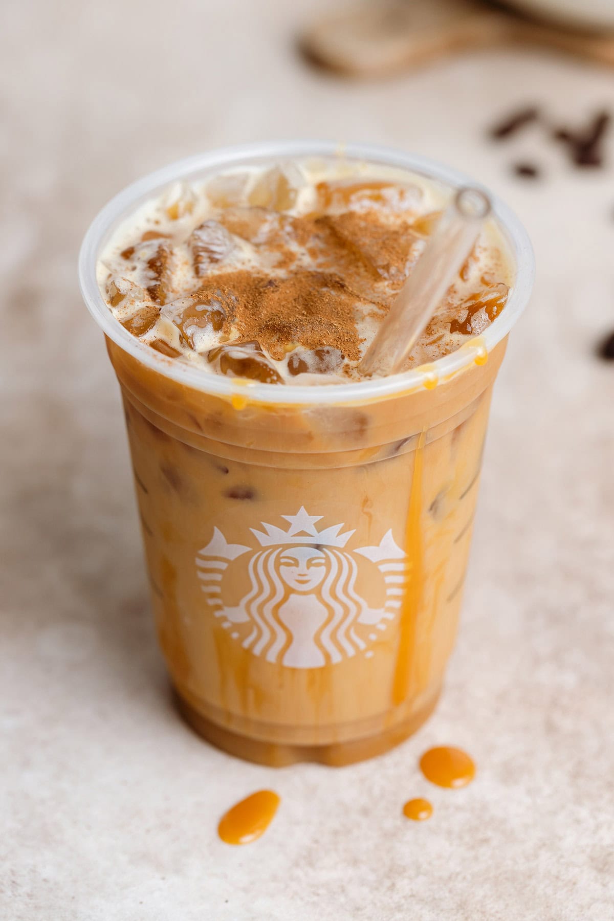 Iced caramel macchiato in a plastic Starbucks cup with a glass straw on a beige background.