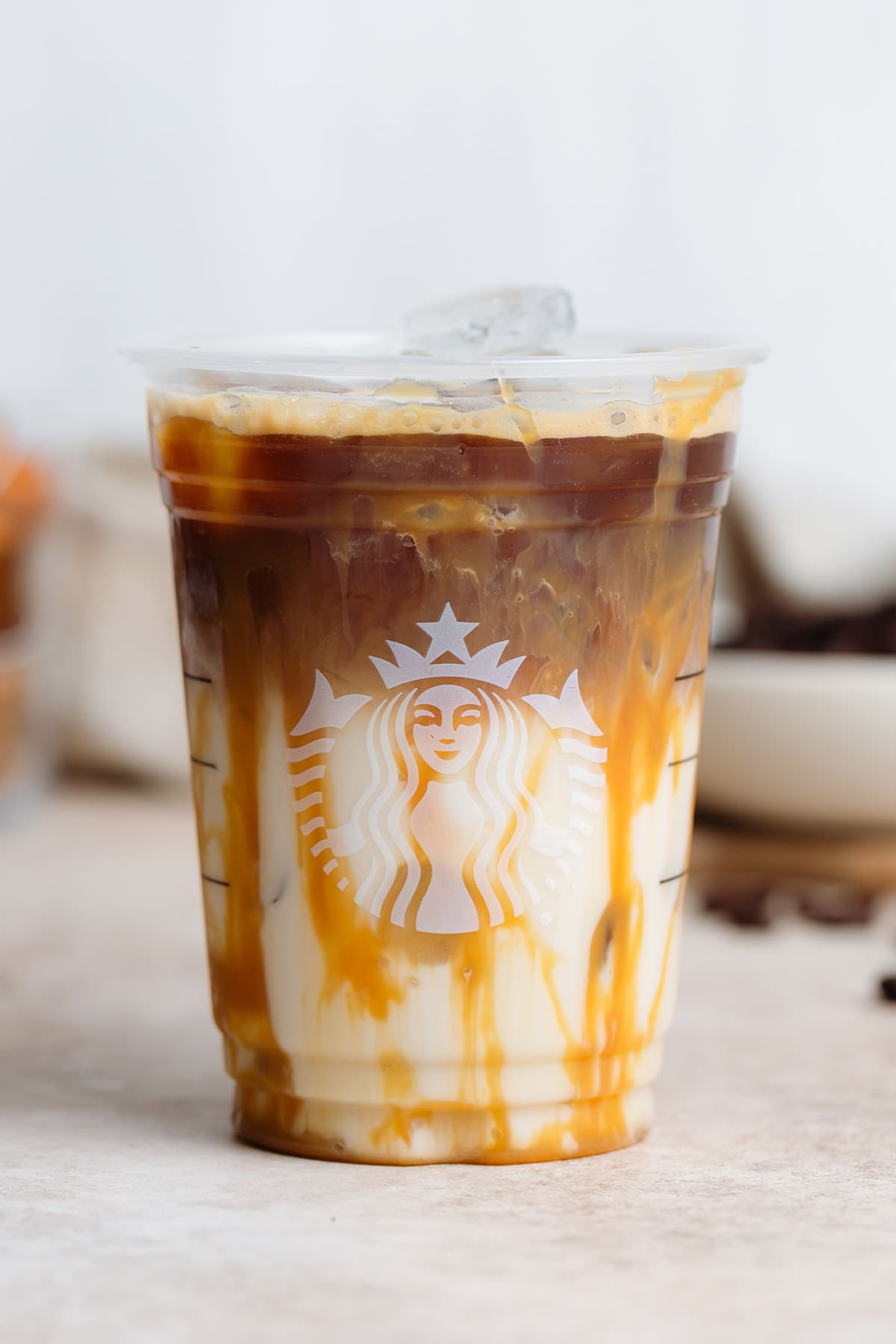 Iced caramel macchiato in a plastic Starbucks cup on a beige background.