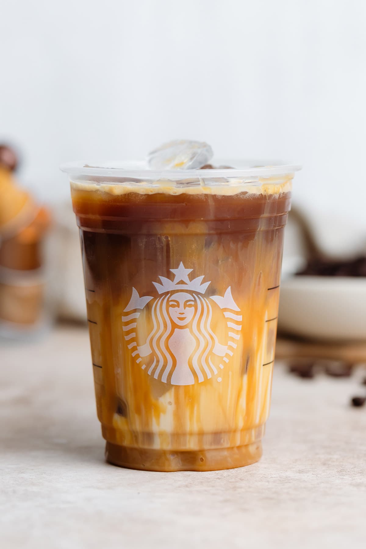 Iced caramel macchiato in a plastic Starbucks cup on a beige background.