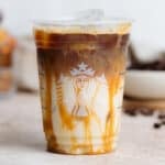 Iced caramel macchiato in a plastic Starbucks cup on a beige background.