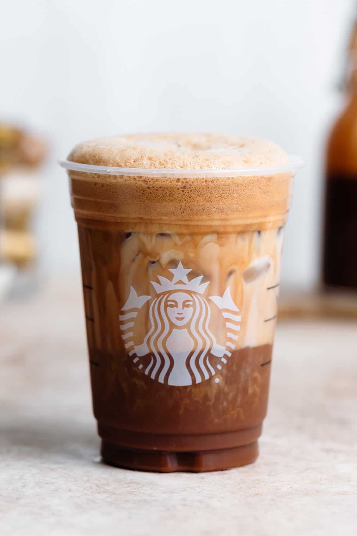 Frothy shaken espresso in a plastic Starbucks cup with milk mixing with the coffee.