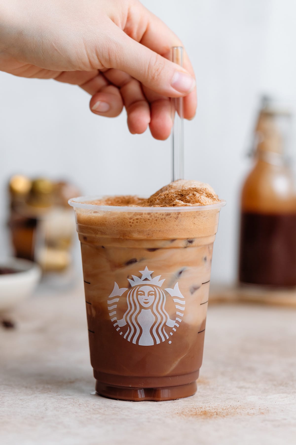 A hand stirring frothy shaken espresso in a plastic Starbucks cup with a glass straw.