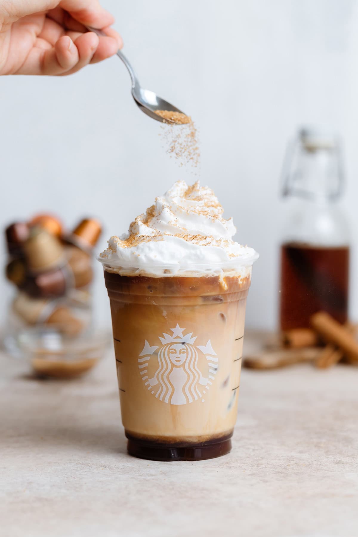 Sprinkling turbinado sugar on iced cinnamon latte with whipped cream.