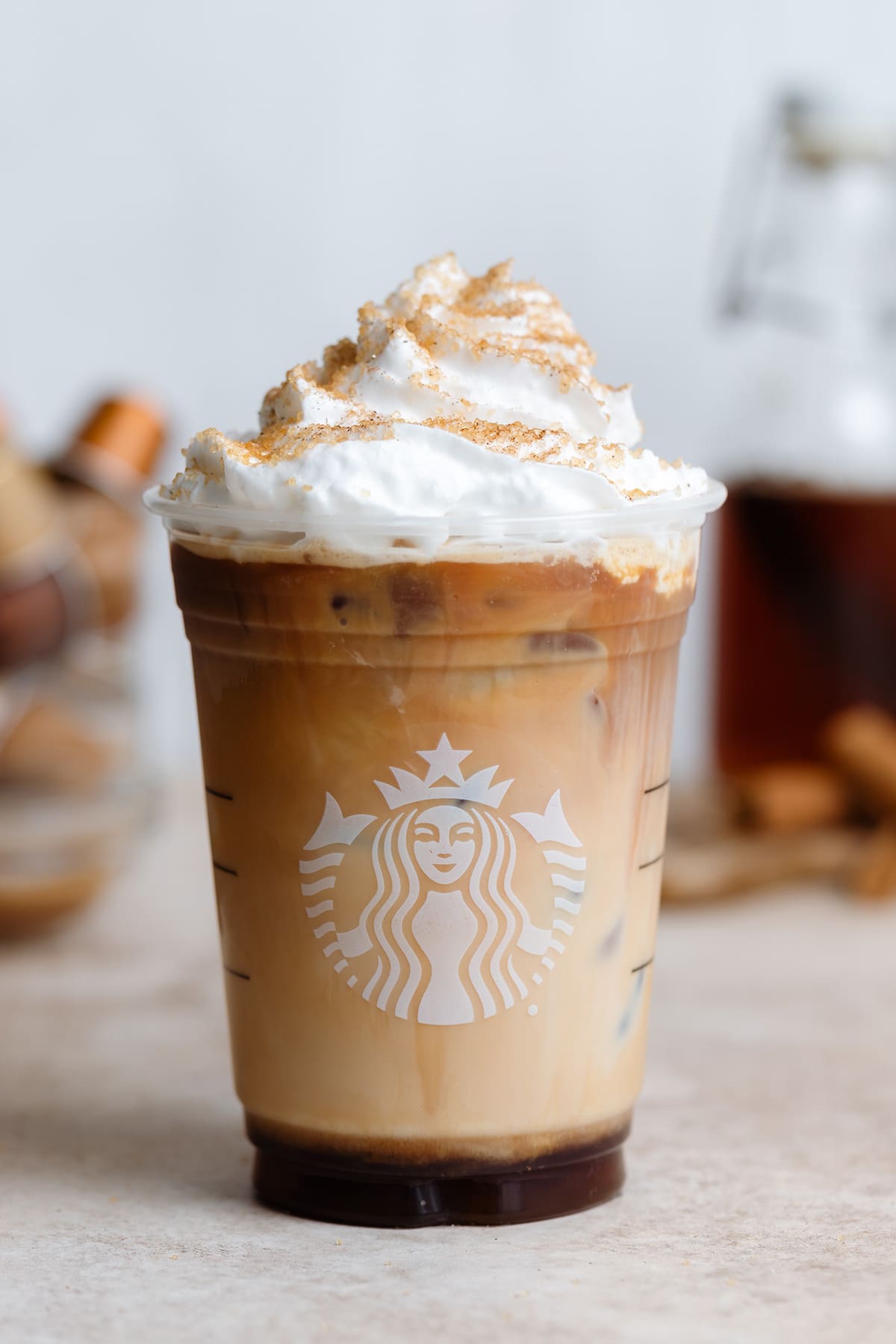 Iced cinnamon latte with whipped cream and sugar sprinkle in a Starbucks cup.