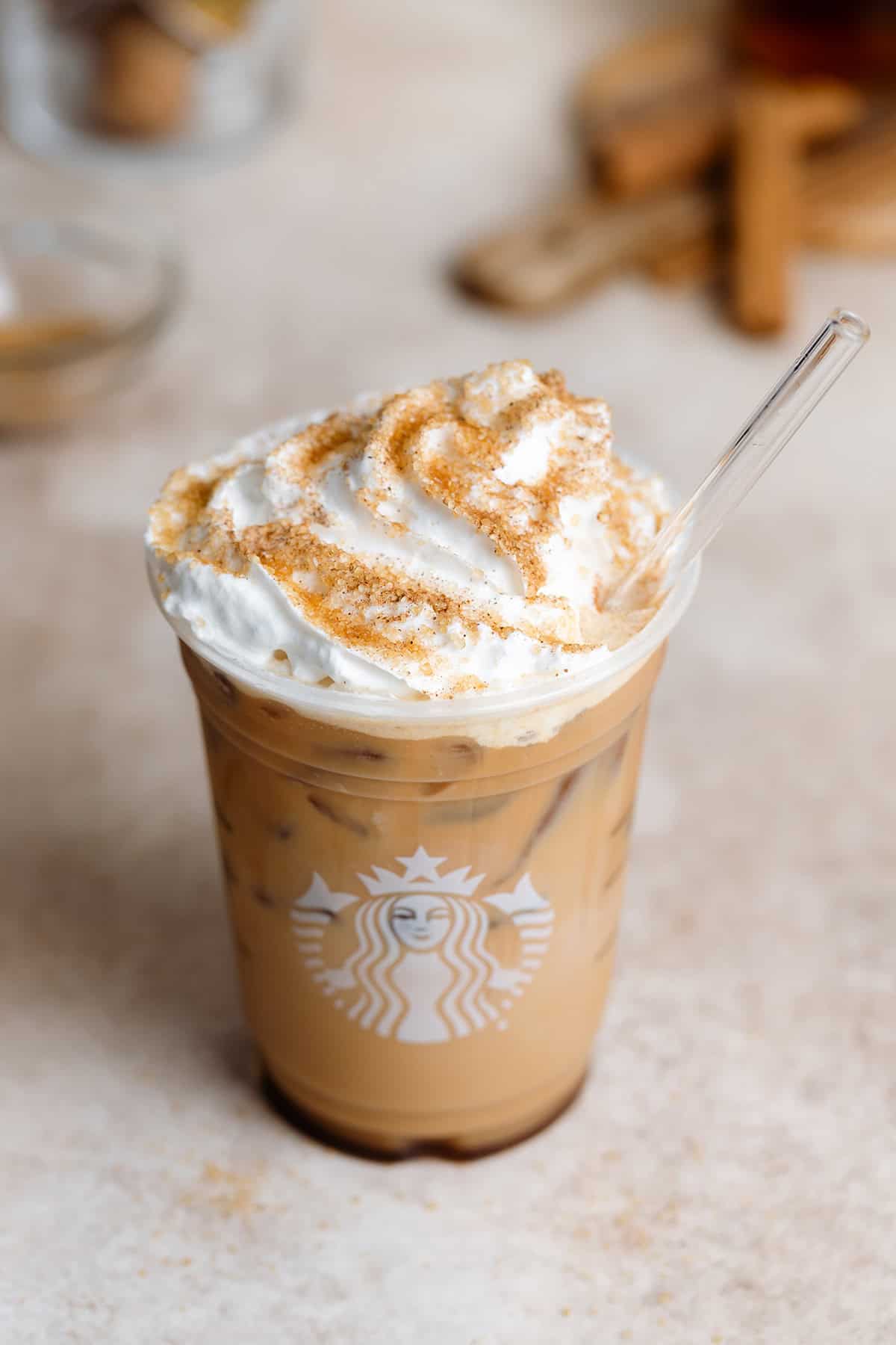 Iced Cinnamon Dolce Latte with whipped cream in a plastic Starbucks cup with a glass straw.