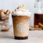Iced cinnamon latte with whipped cream and sugar sprinkle in a Starbucks cup.