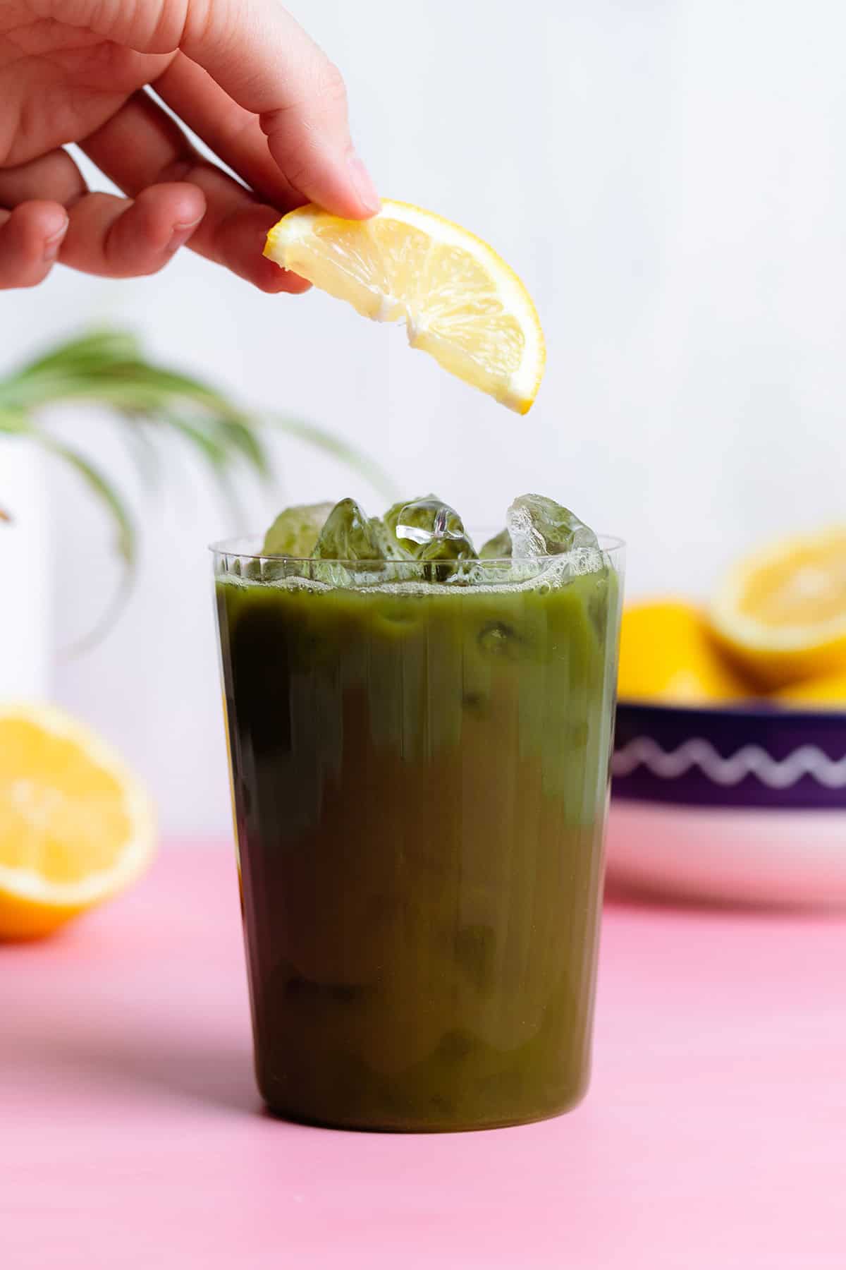 A hand placing a lemon slice on a tall glass with iced matcha lemonade.