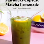 Matcha lemonade with a lemon slice in a tall glass with a glass straw on a pink background.