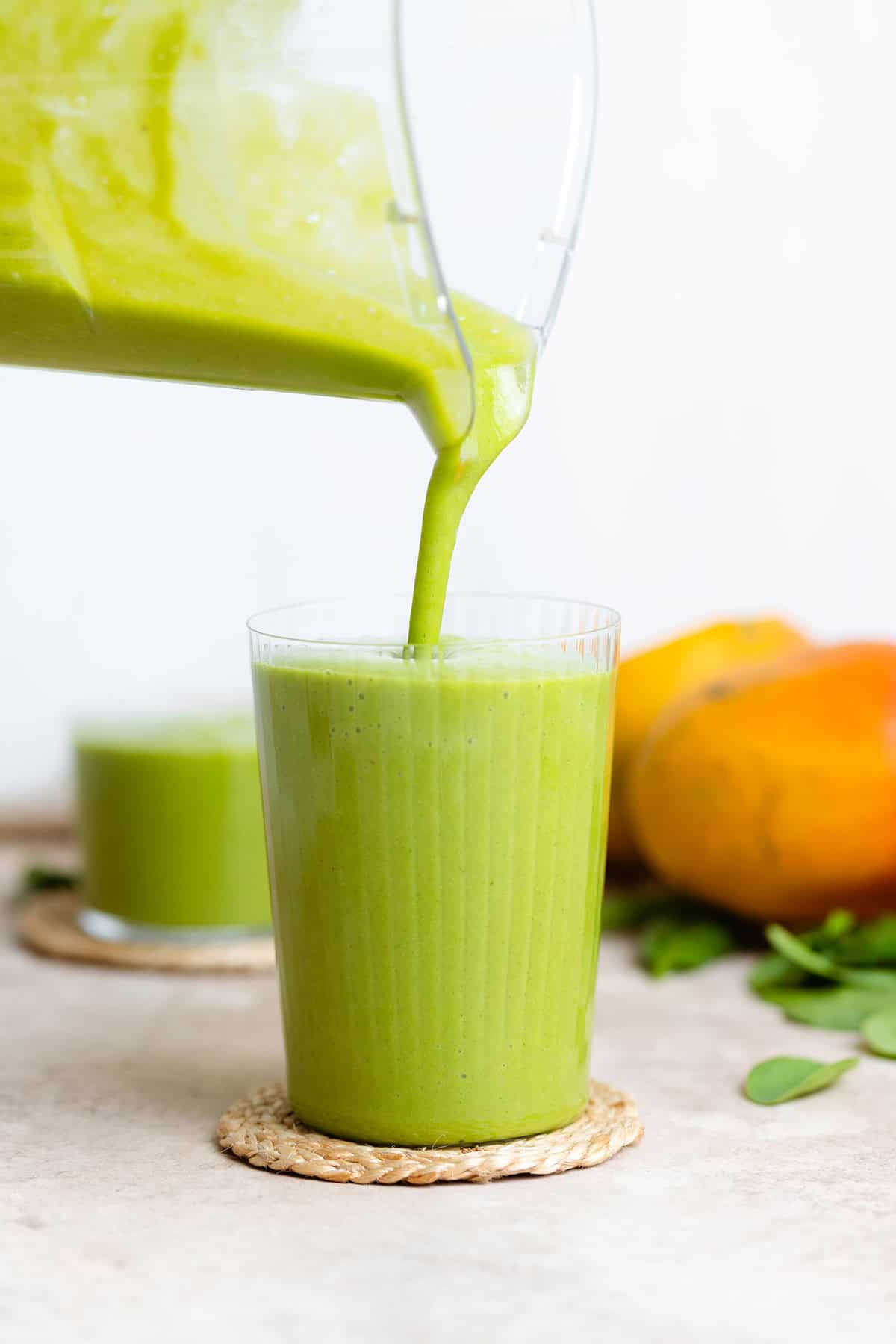 Green smoothie being poured into a tall glass out of a blender.