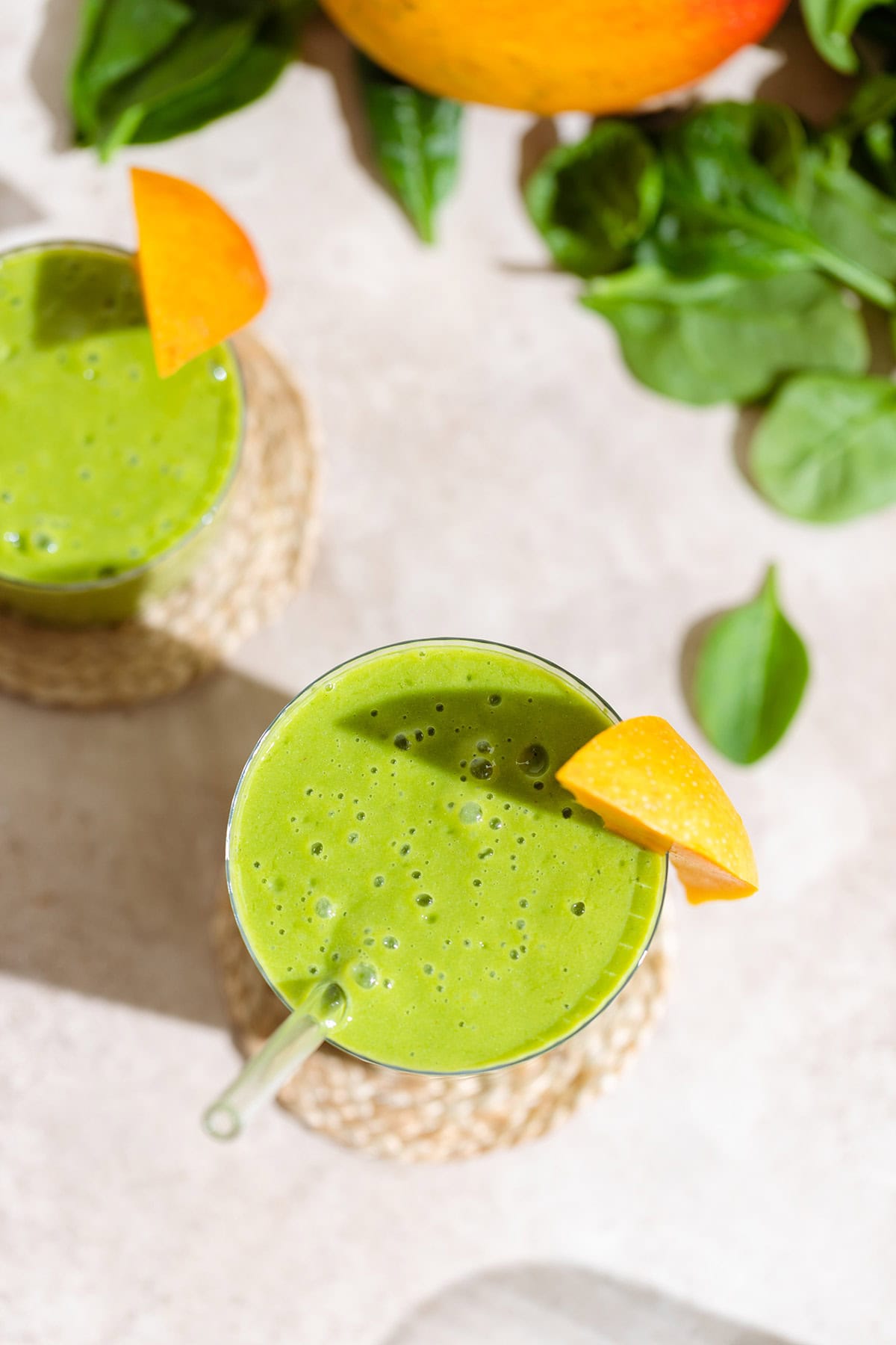 Green smoothie in a tall glass shot from above, garnished with a slice of mango.