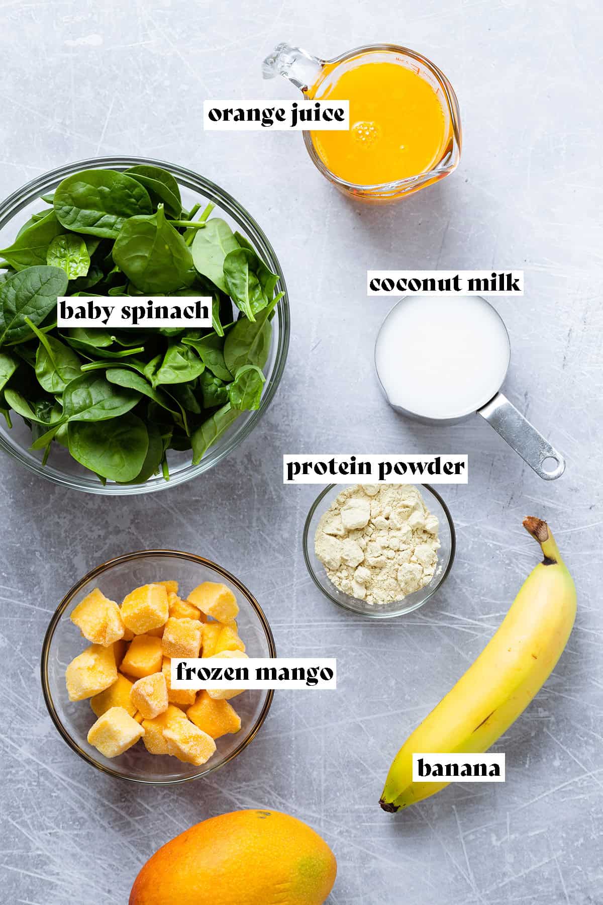 Ingredients for a mango spinach smoothie all laid out like baby spinach, frozen mango, and orange juice.